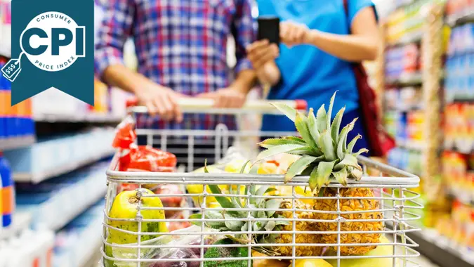 Close-up of fruits in shopping cart with couple using smart phone at grocery store.