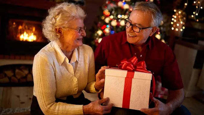 Happy grandparents smiling and holding big gift at Christmas eve.