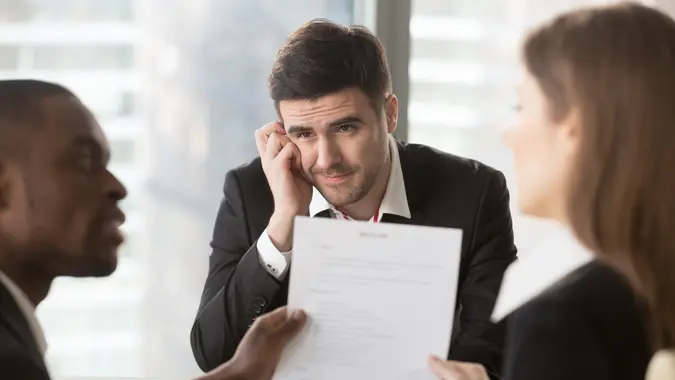 Worried male job candidate interested in company vacancy anxiously looking on multinational recruiters analyzing and discussing his resume on interview.