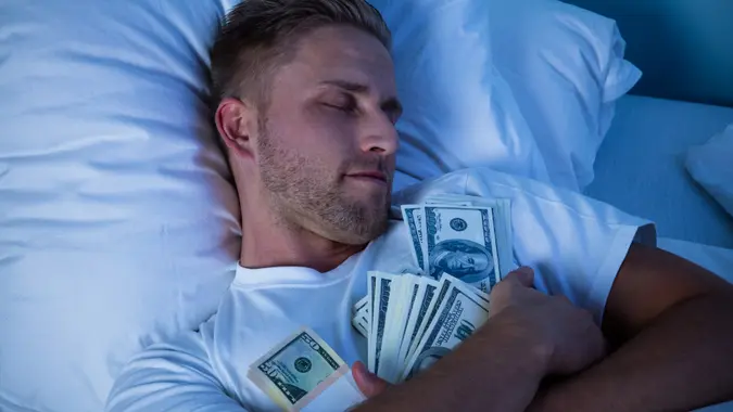 Man Sleeping On Bed With Bundle Of Currency Notes.
