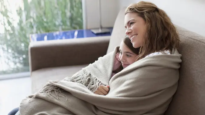 Mother and daughter wrapped in blanket on couch stock photo