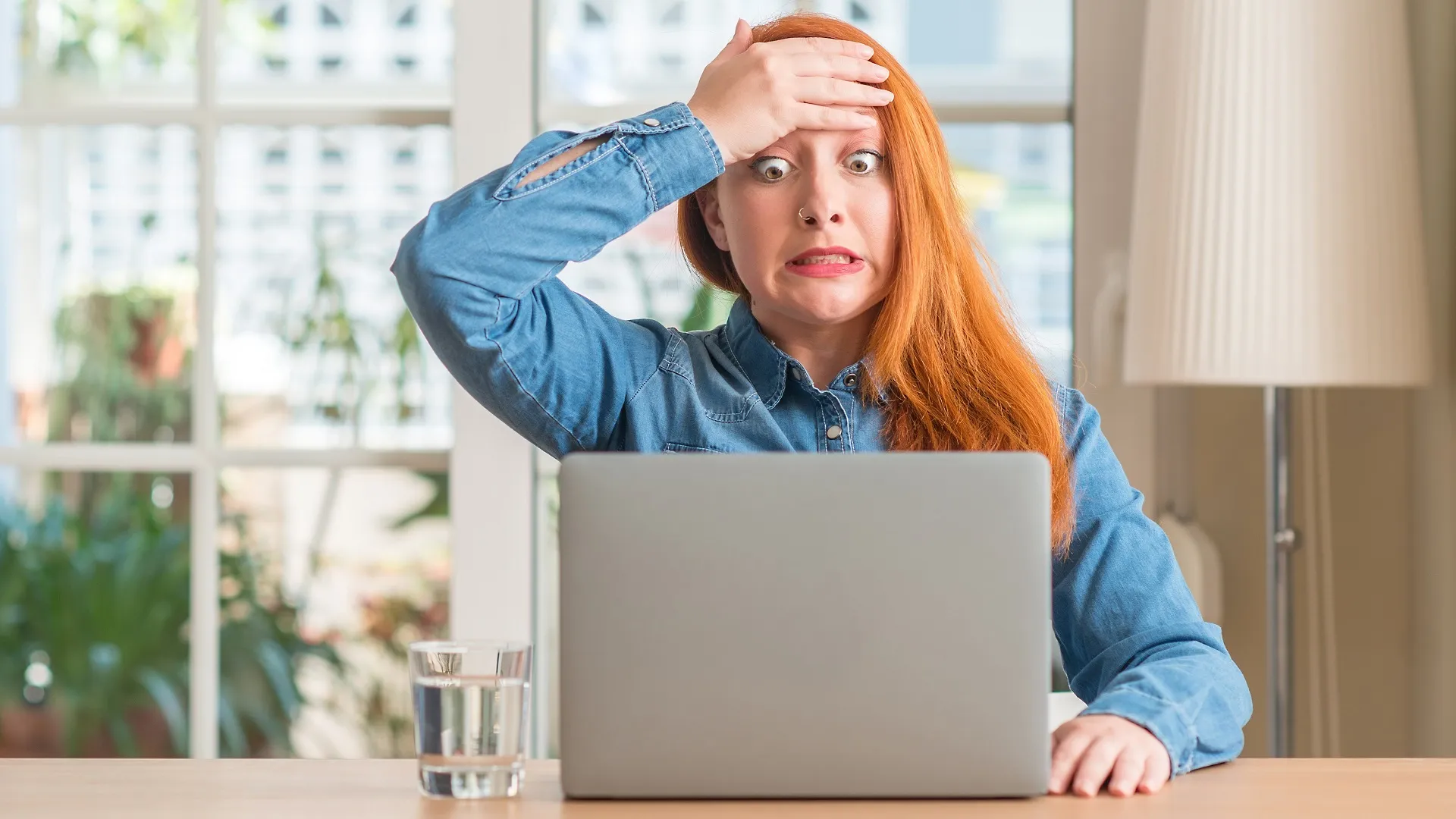 Redhead woman using computer laptop at home stressed with hand on head, shocked with shame and surprise face, angry and frustrated. Fear and upset for mistake. stock photo