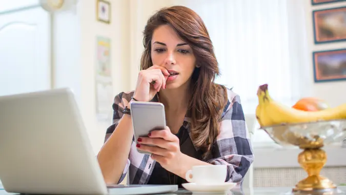 Young nervous woman looking at smartphone and biting her fingernails at home. stock photo