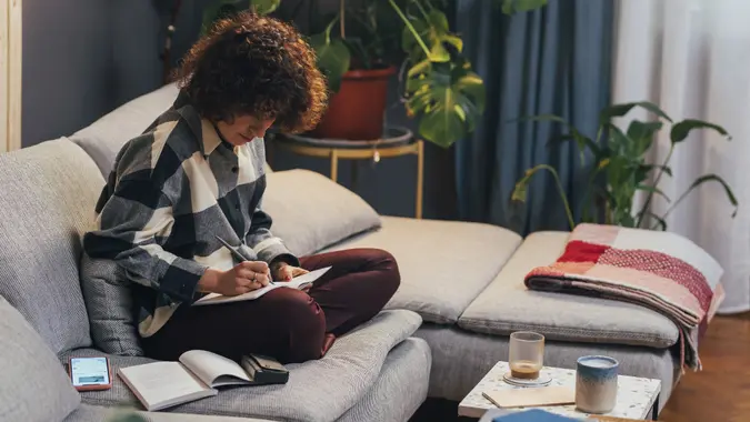 Young Caucasian Woman with Curly Hair Sitting in her Living Room and Making a To-Do List stock photo