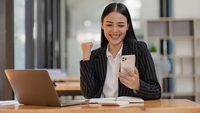 Asian businesswoman holding a smartphone analyzing a report pointing to a graph with a pen, laptop, and calculator. in workstation accountant telemarketing ideas ecommerce free online marketing stock photo