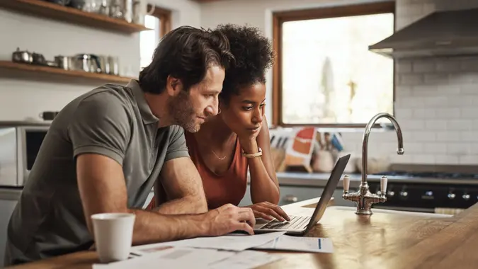 Cropped shot of couple doing paperwork at home using laptop.