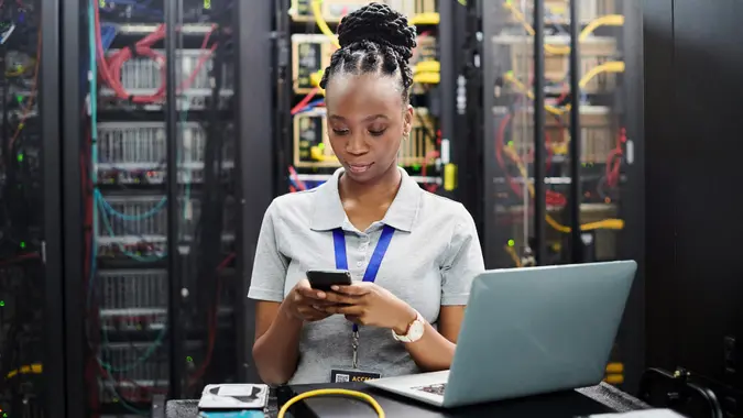 Shot of a young woman using a cellphone while working in a server room stock photo