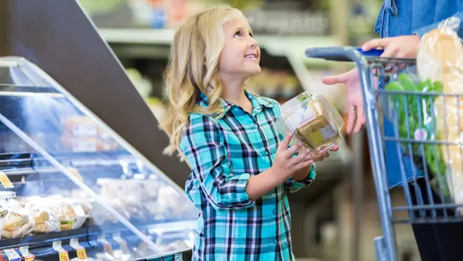 Little girl shopping at deli in grocery store with mom stock photo