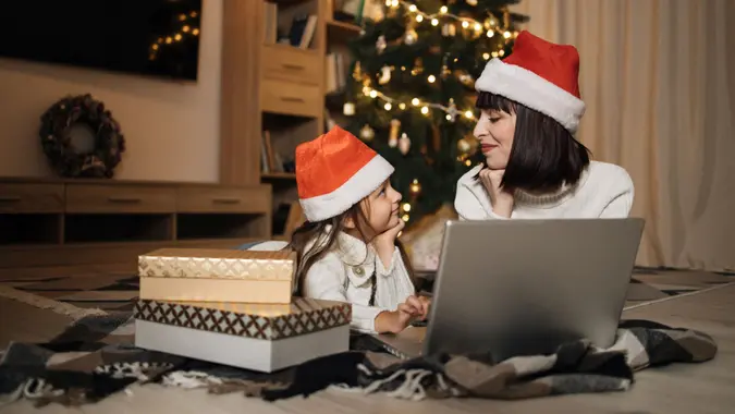 Indoor shot of beautiful happy young woman and her girl shopping online on laptop in cozy Christmas interior.