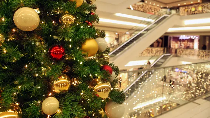 Close up of a Christmas tree with decorations and lights, ornating a modern shopping mall main space, out of focus, with lights, stairs and escalators on the background, modern architecture.