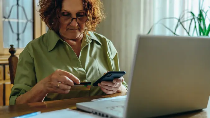 Senior woman using a smartphone and a credit card at home stock photo