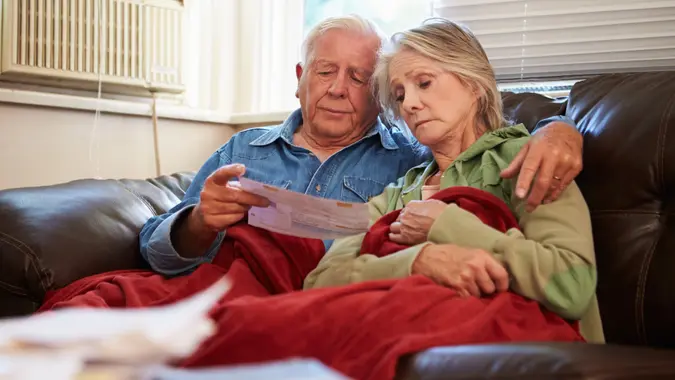 Worried Senior Couple Sitting On Sofa Looking At Bills stock photo
