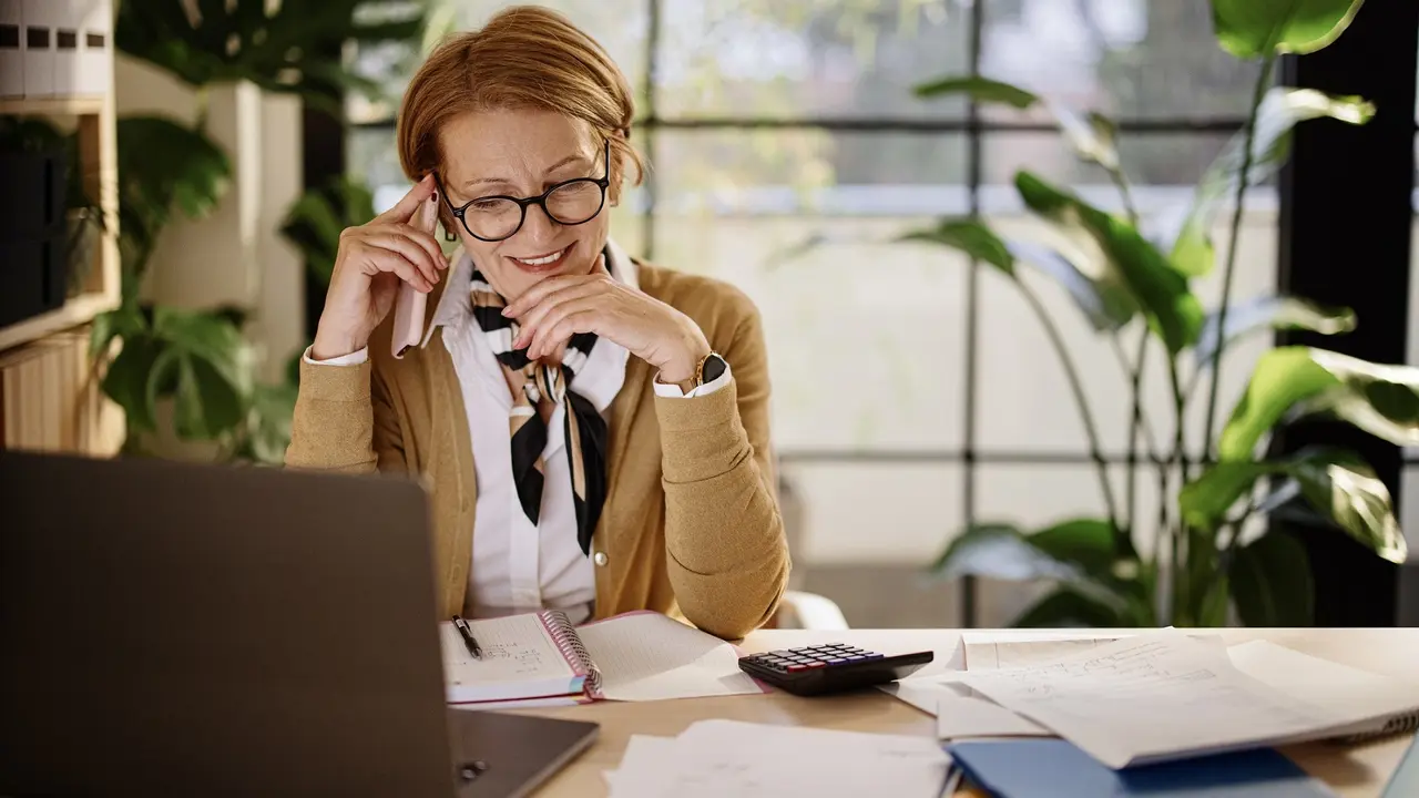 Happy businesswoman using mobile and laptop while working at home stock photo