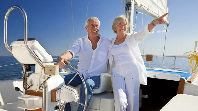 A happy senior couple sitting at the wheel of a sail boat on a calm blue sea.