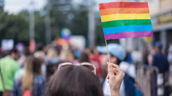 Rear view image of young woman waving rainbow colored flag at street parade.