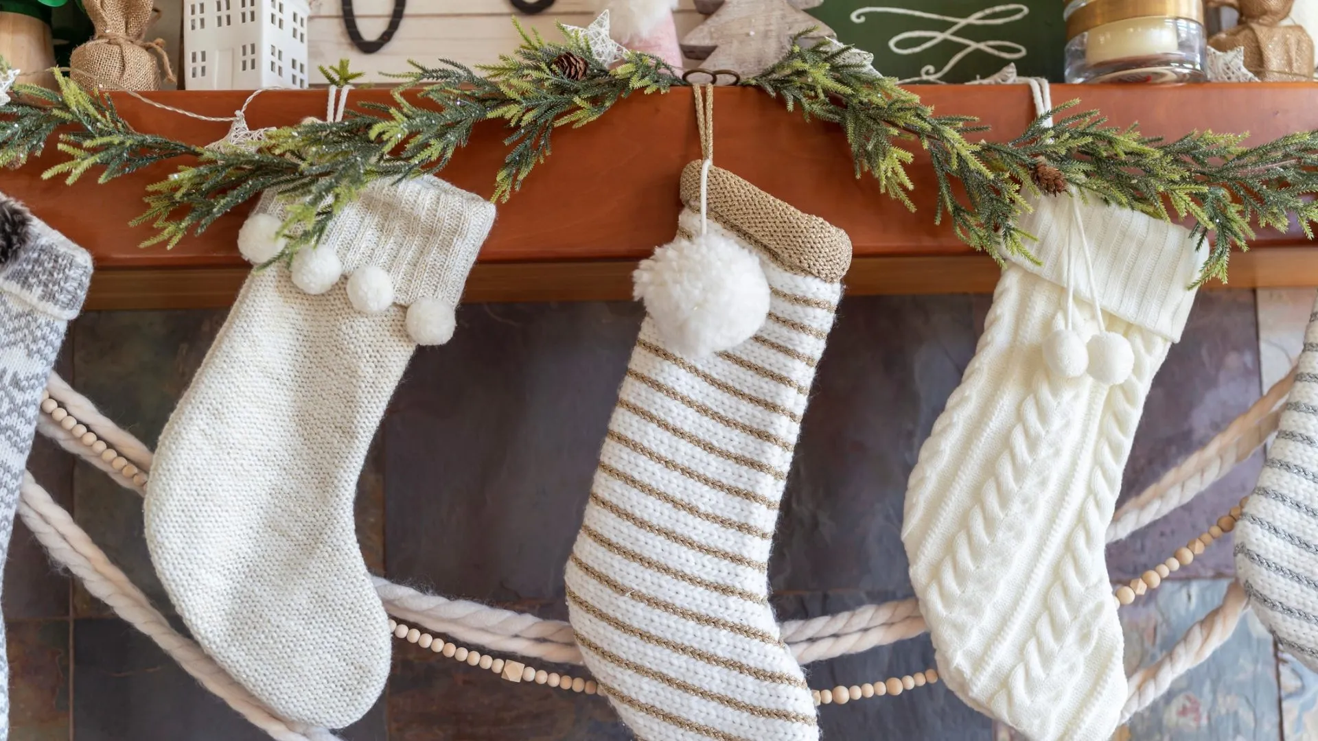 Close up of white Christmas stockings and winter holiday decorations in modern farmhouse Scandinavian design above fireplace in cozy family living room.