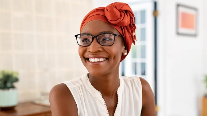 Cheerful mature black woman wearing spectacles and traditional turban at home.