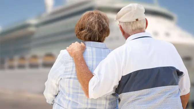 Senior Couple On Shore Facing and Looking at Docked Cruise Ship.