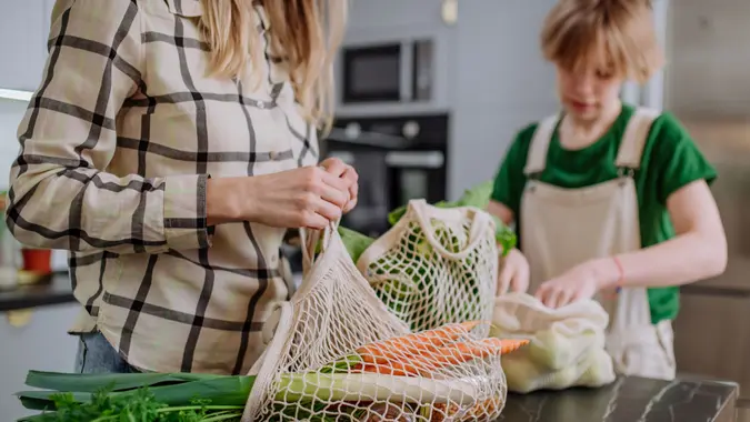 A mother unpacking local food in zero waste packaging from bag with help of daughter in kitchen at home.