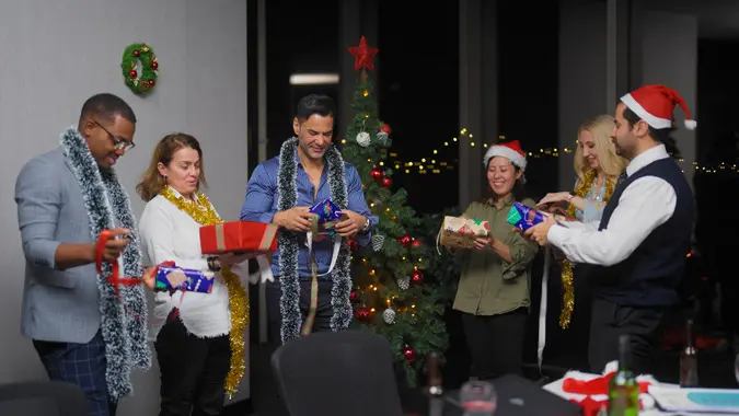 A group of a multiracial business people are celebrating Christmas and opening Christmas presents at the office.
