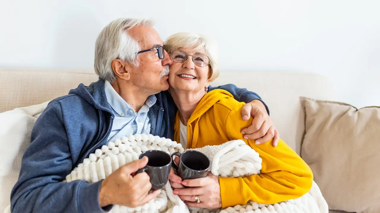 Senior couple feeling cozy and warm, sitting covered with blanket on the sofa at home.