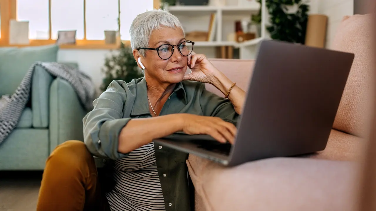 Senior woman using laptop on living room floor stock photo
