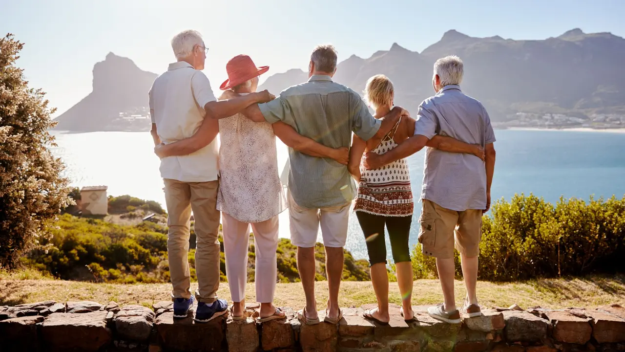 Rear View Of Senior Friends Visiting Tourist Landmark On Group Vacation Standing On Wall.