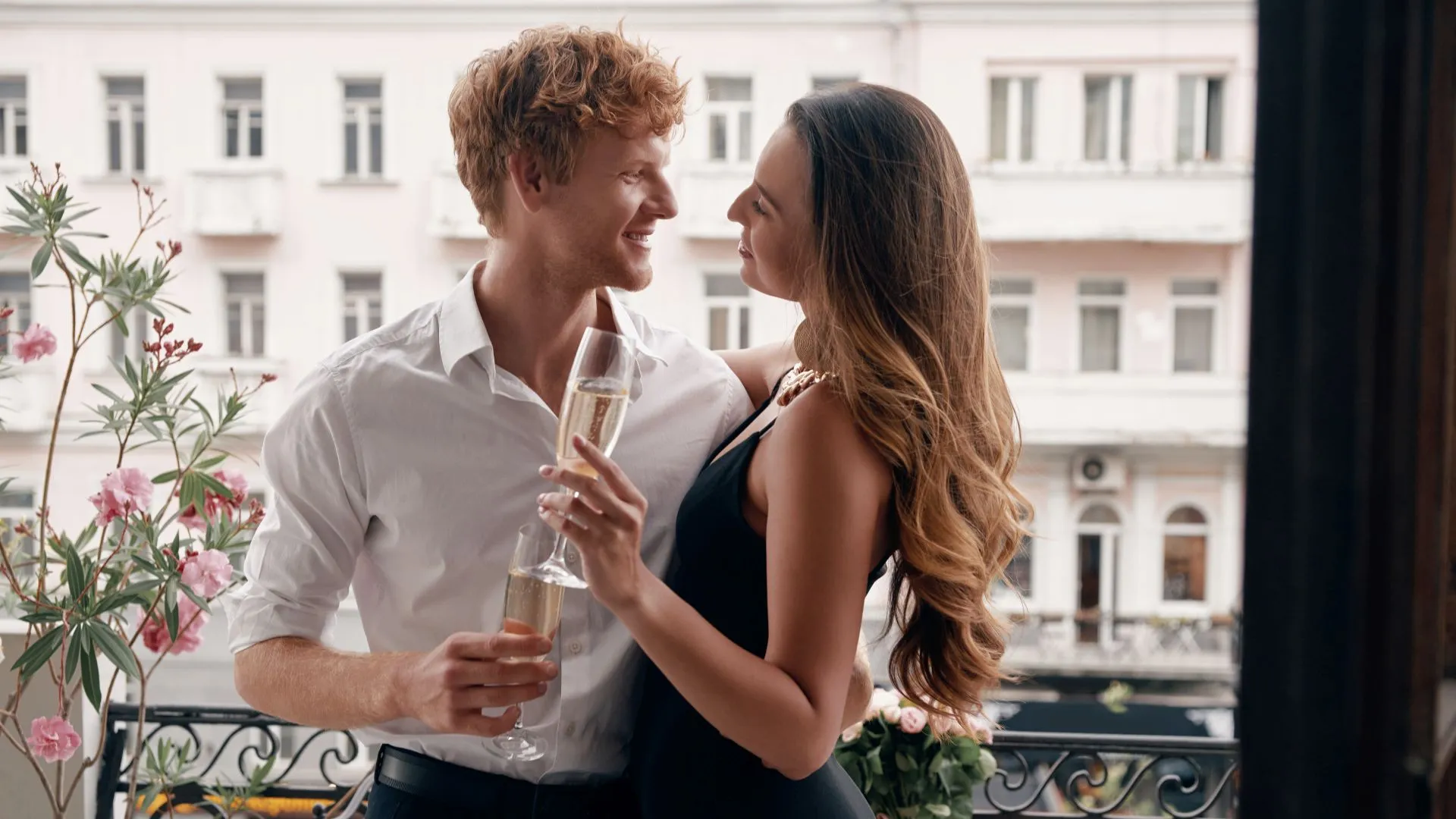 Happy young couple in formalwear embracing while enjoying champagne on the balcony together.
