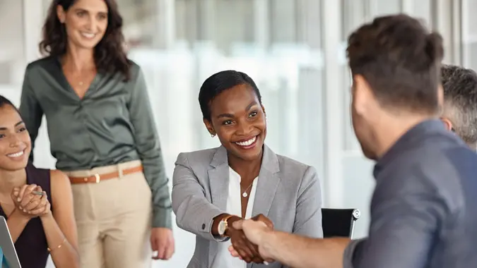 Happy black businesswoman and businessman shaking hands at meeting.