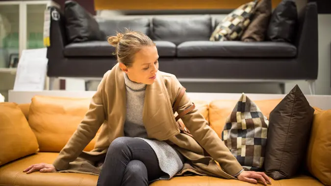 A young woman sits on a couch while shopping for furniture.