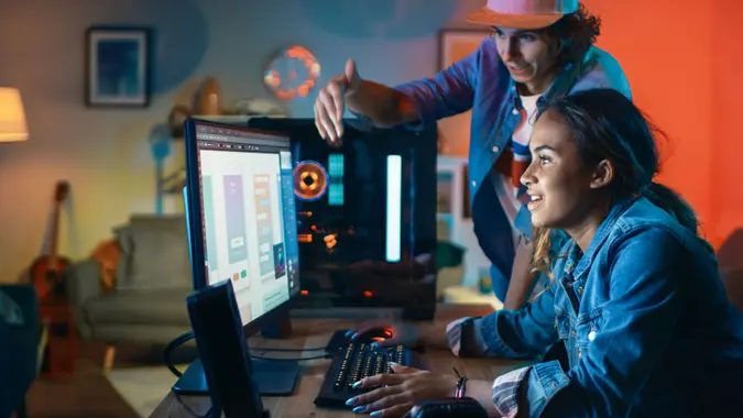 Two Friends or a Couple Discuss Mobile Design Interface on a Computer Screen.