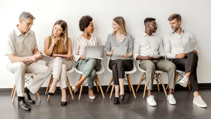 Multicultural diverse candidates sit on chairs wait for interview have fun talking, happy multiethnic diverse applicants speak and chat joke laugh before hiring process, employment concept.