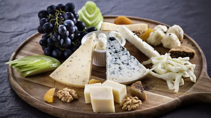 Variety of cheeses and grapes on wooden board.