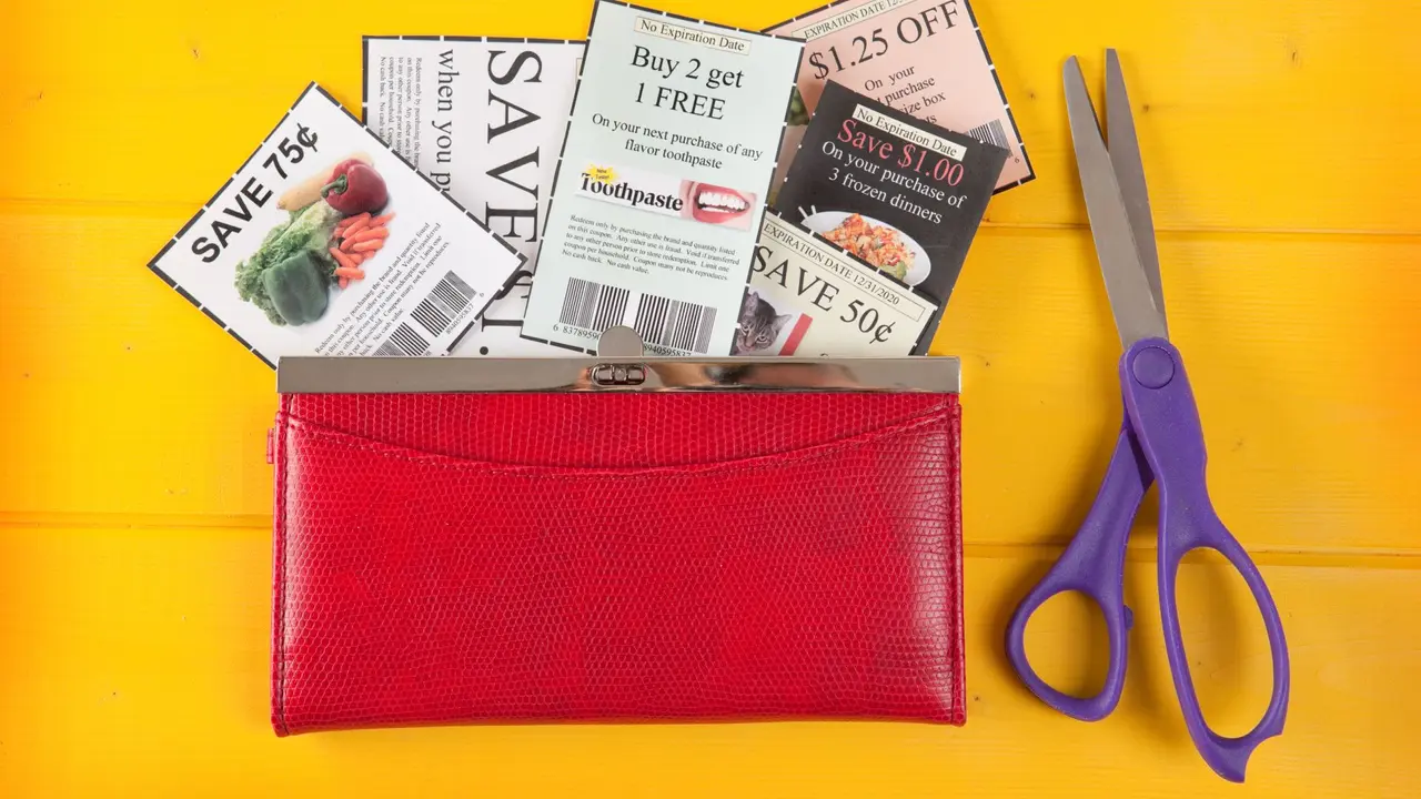 Coupons in a wallet with a pair of scissors resting on a yellow table.