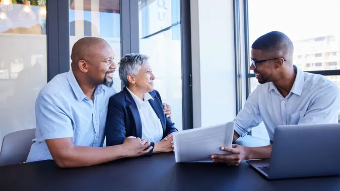 Smiling young financial advisor going over documents with a mature couple during a meeting together at a table in his office.