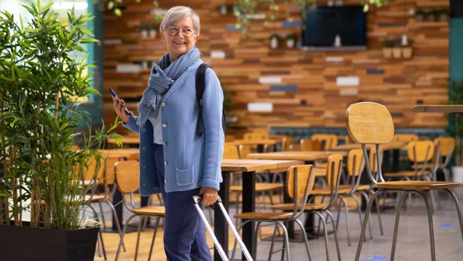 Smiling caucasian traveler senior woman with backpack and hand luggage walking in airport waiting for departure flight.