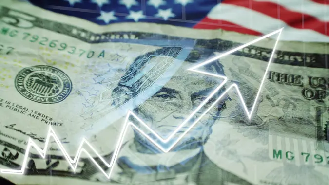 Business & Finance Concept With Five Dollar Bill, American Flag & Stock Graph Showing Bull Market High Quality Stock Photo.