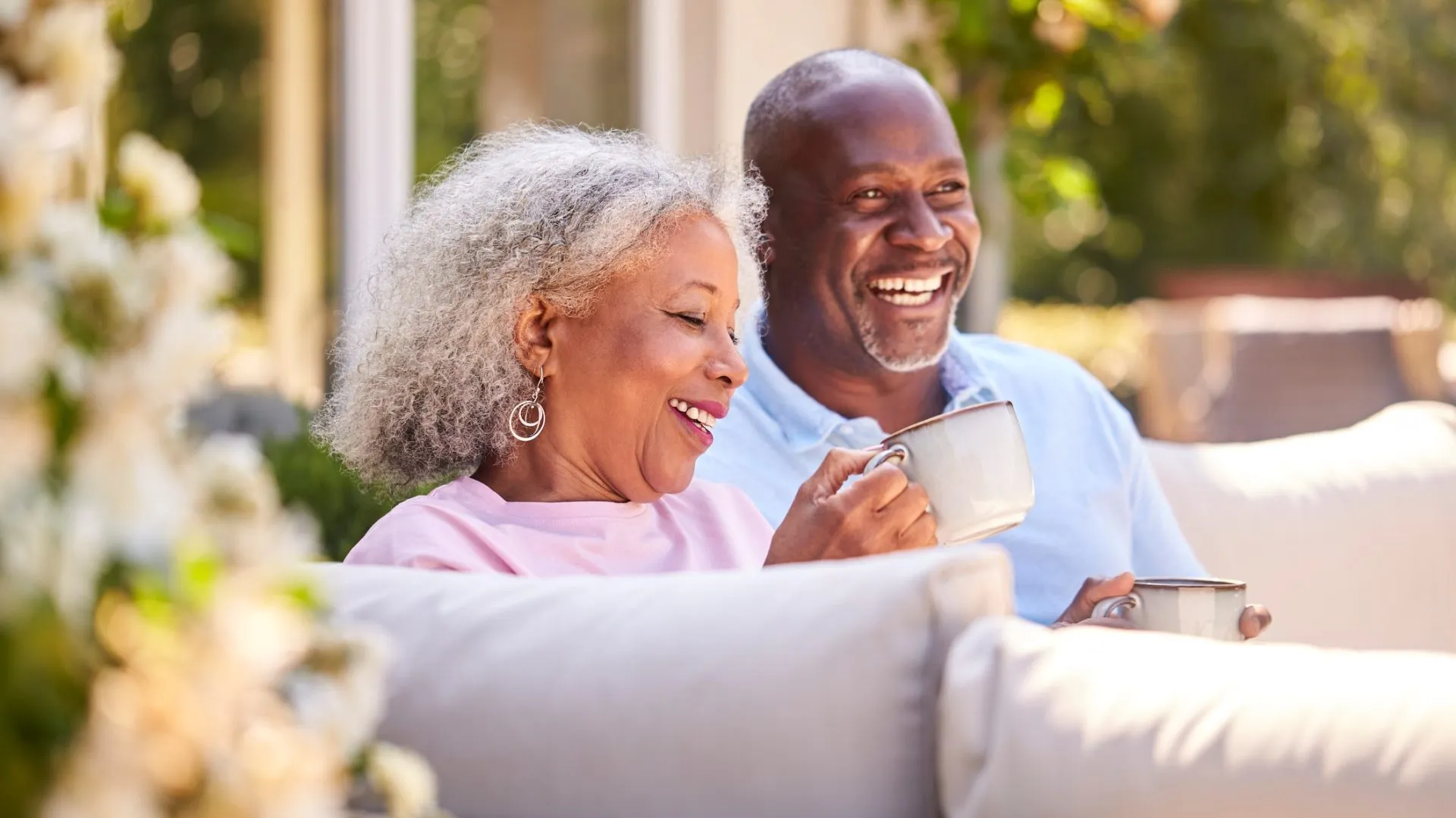 Retired Couple Sitting Outdoors At Home Having Morning Coffee Together.