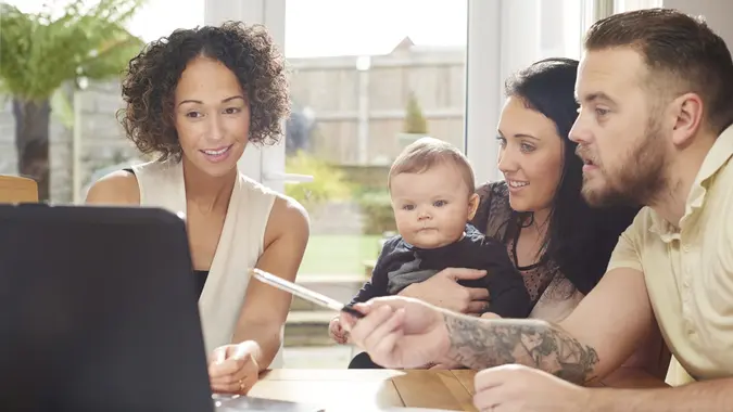 a young husband and wife with their baby sit and chat to a woman in their dining room .