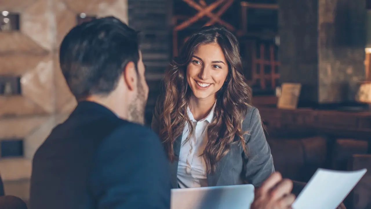 Two people in formal businesswear talking and smiling.