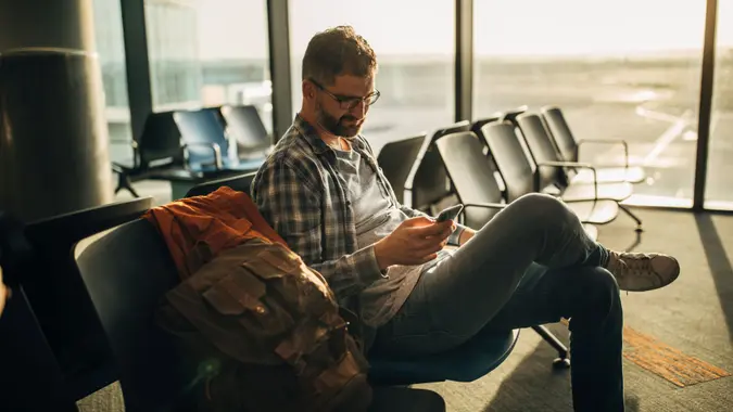 One man, gentleman sitting in waiting room on airport, using smart phone.