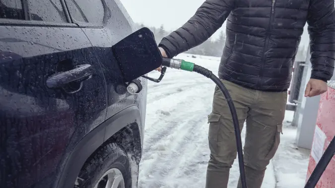 During a cold winter and snowy day, a man pours gasoline into a car. ISL stock photo