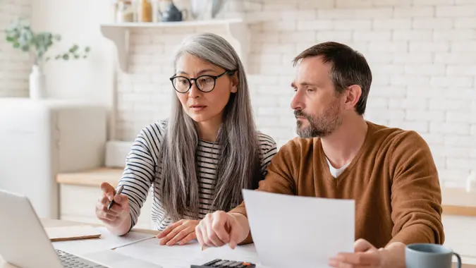 Mature middle-aged couple family wife and husband counting funds, savings declarations, investments,paperwork, financial documents, bankruptcy, court case, bills, pension with laptop.