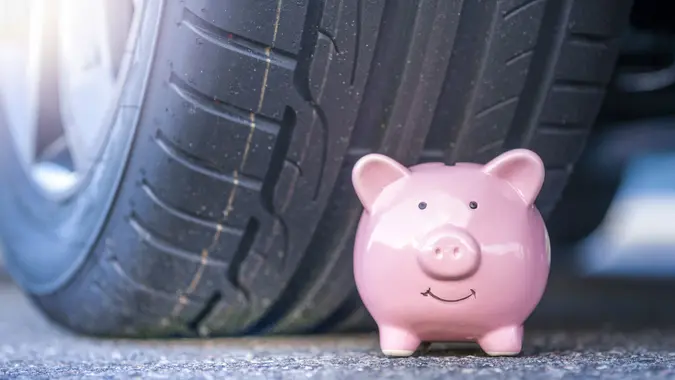 Pink piggy bank sits next to the new tire of a modern car stock photo