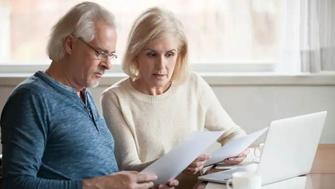 Serious worried senior couple calculating bills to pay or checking domestic finances stressed of debt, retired elderly old family reading documents concerned about loan bankruptcy money problems.