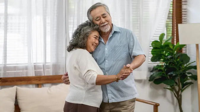 A senior couple dancing and hugging each other in their living room at home.