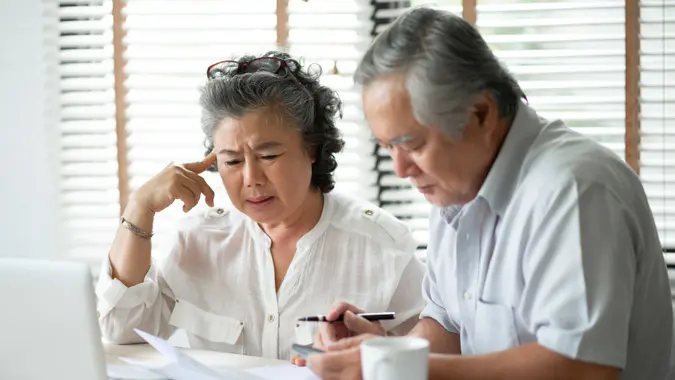 Serious Asian Senior Couple thinking about their Debts with laptop computer.