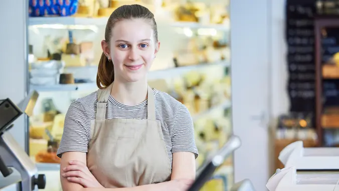 Portrait Ot Teenage Girl Working In Delicatessen Food Shop As Job Experience.