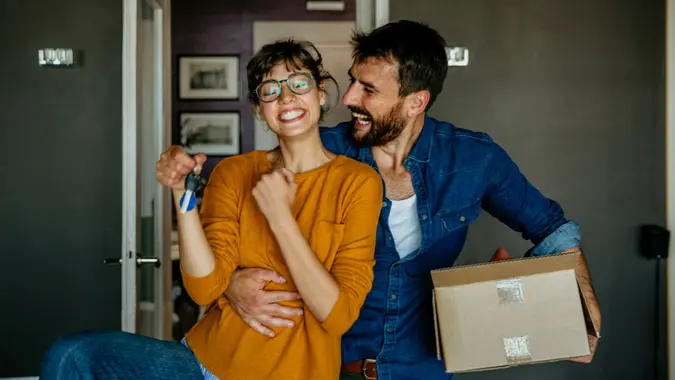 Portrait of a happy woman and a man, holding keys from the new first house, a young family of two celebrating moving day, satisfied customers couple purchase real estate, mortgage, and relocation concept.