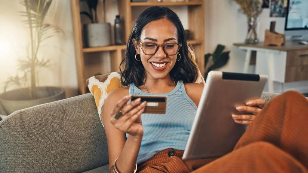 微笑的混血妇女使用信用卡在家里的数字平板电脑上进行电子商务。